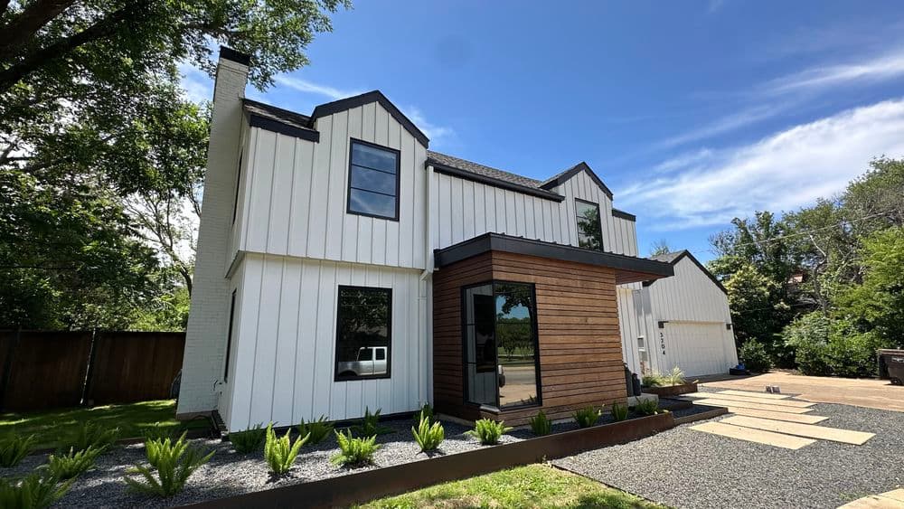 Modern two-story home with white and wooden exterior, landscaped yard, and blue sky.