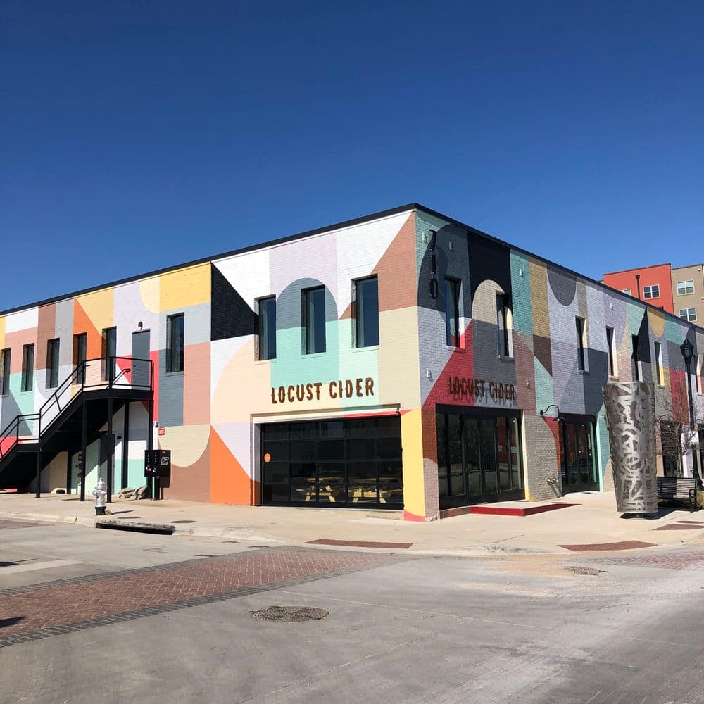 Colorful exterior of Locust Cider building with mural, located in a vibrant urban setting.